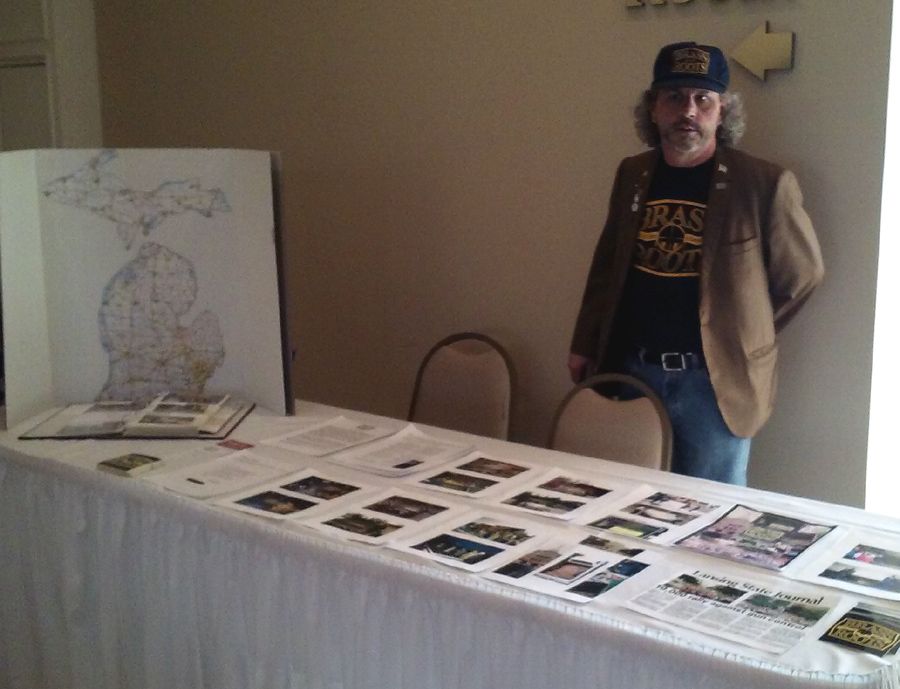 Brass Roots Director Mike Hoban shows off photographs that chronicle the journey the Brass Roots Plaque took around the state, along with a map of Michigan covered in brass tacks that mark where it has been.